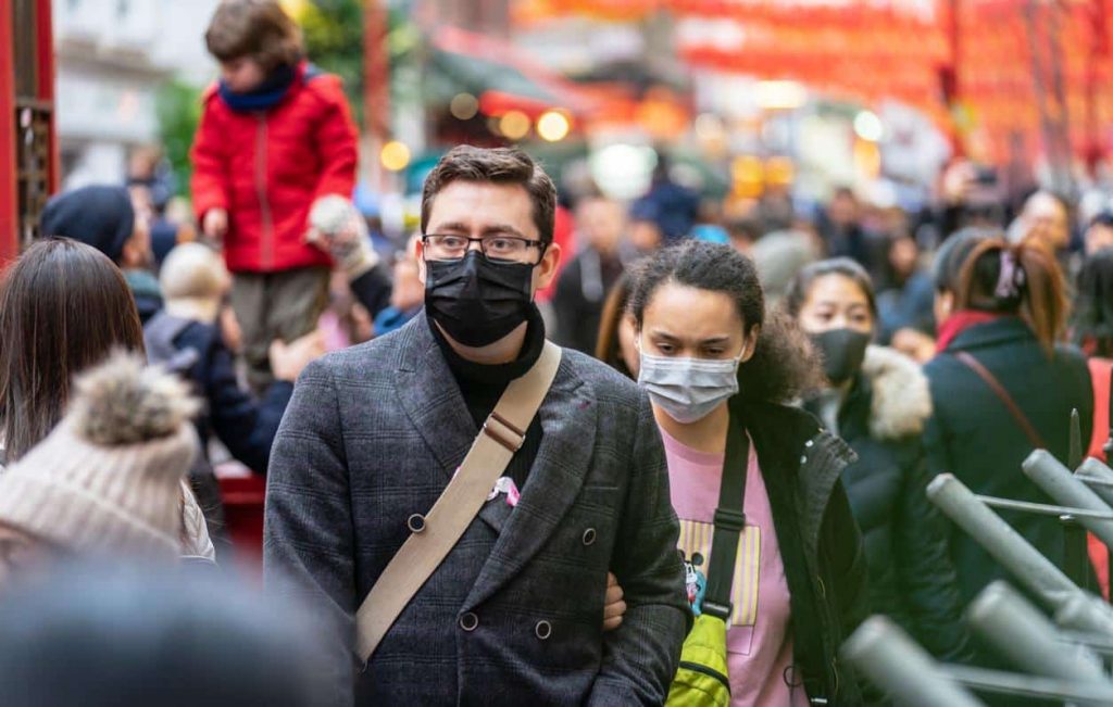 População andando na rua utilizando máscara. 